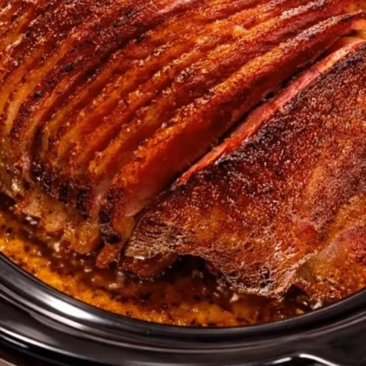 A beautifully caramelized spiral-cut ham glistening with sweet brown sugar glaze inside a black slow cooker