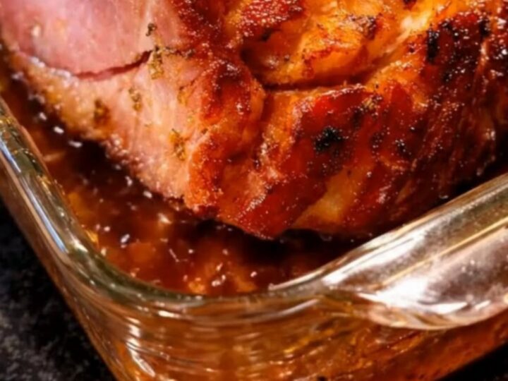 A beautifully glazed baked ham with a glistening caramelized crust, resting in a glass baking dish with rich pan juices.