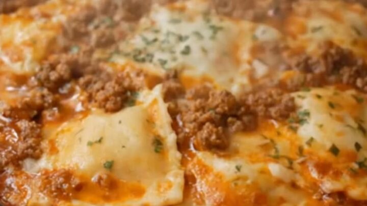 A serving spoon lifting a cheesy portion of slow cooker ravioli lasagna with an impressive mozzarella cheese pull.