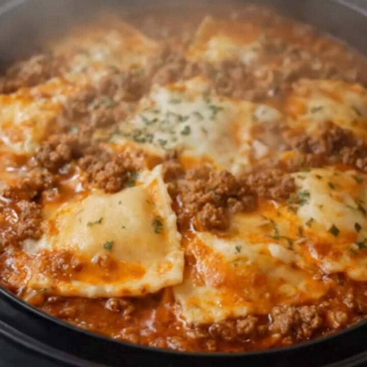 A serving spoon lifting a cheesy portion of slow cooker ravioli lasagna with an impressive mozzarella cheese pull.