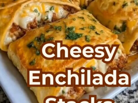 A spatula lifting a cheesy beef enchilada stack from a white casserole dish with a dramatic cheese pull.