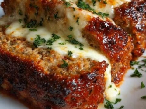 A thick slice of glazed French onion meatloaf topped with melted bubbly cheese and fresh parsley on a platter.