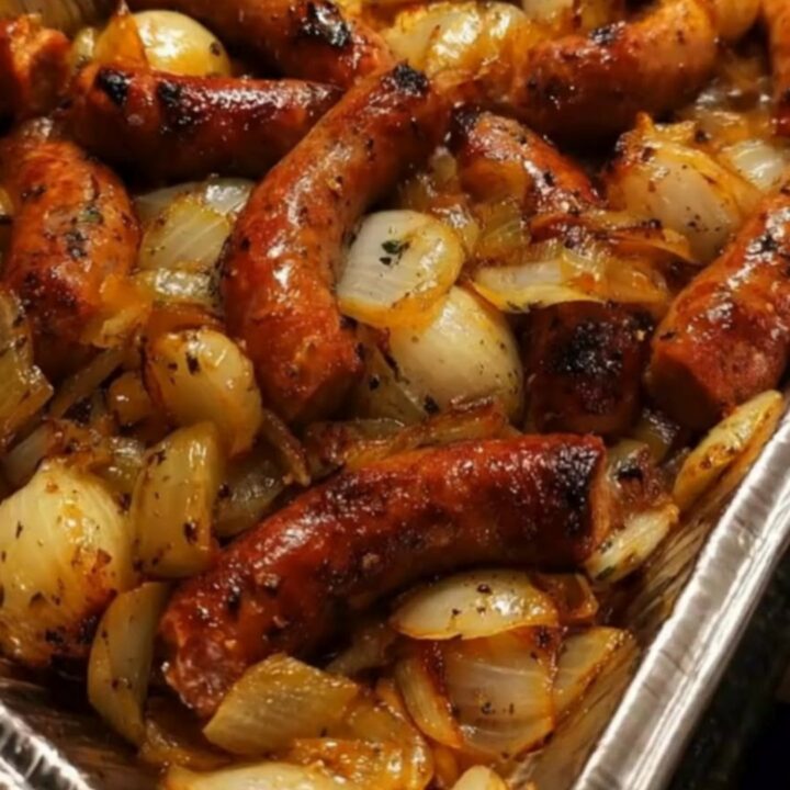 A close-up of glistening, charred smoked sausage pieces and caramelized onions in a sticky honey barbecue glaze.