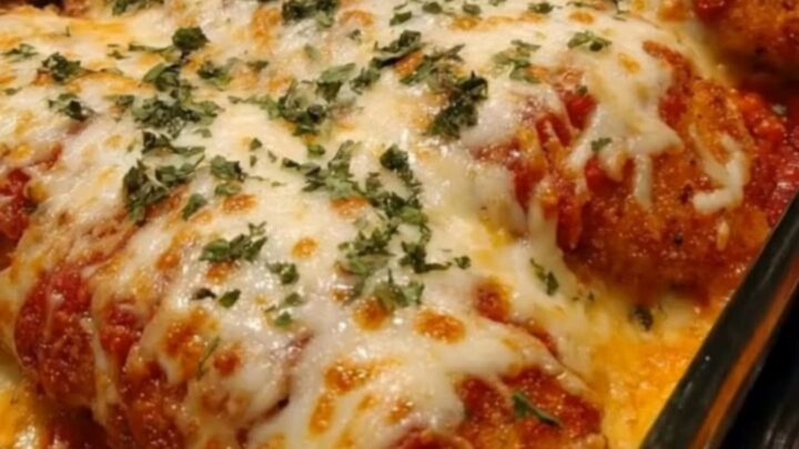 Baked chicken cutlets in a glass casserole dish topped with bubbly melted mozzarella and parsley