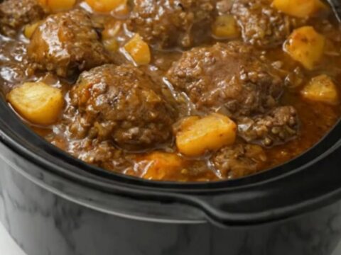 A black slow cooker filled with tender Salisbury steak patties and diced potatoes in rich onion gravy.