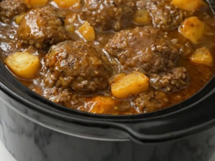A black slow cooker filled with tender Salisbury steak patties and diced potatoes in rich onion gravy.