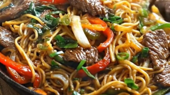 A steaming cast iron skillet loaded with glossy Mongolian beef noodles, tender steak slices, and bell peppers.