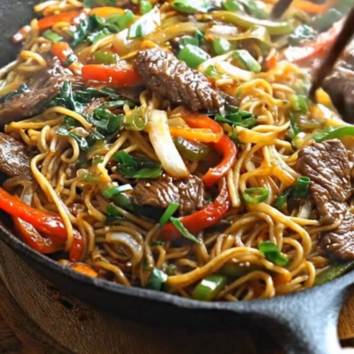 A steaming cast iron skillet loaded with glossy Mongolian beef noodles, tender steak slices, and bell peppers.