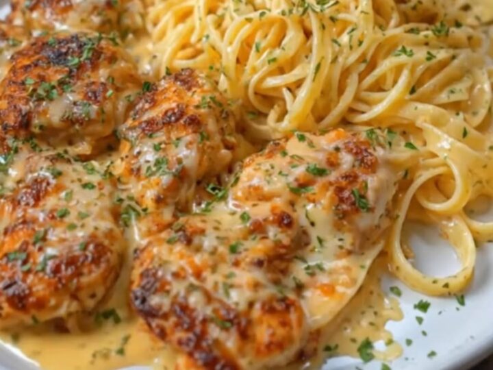 A plate of creamy parmesan fettuccine topped with golden-brown garlic butter chicken bites and fresh parsley.