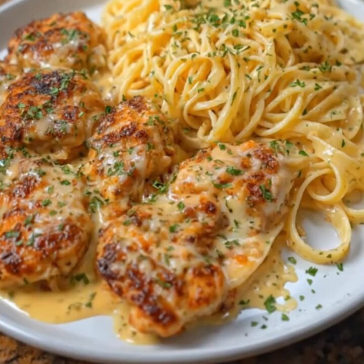 A plate of creamy parmesan fettuccine topped with golden-brown garlic butter chicken bites and fresh parsley.
