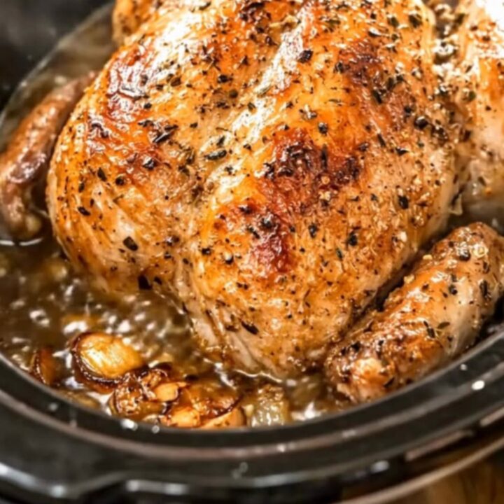 A glistening, golden slow cooker whole chicken seasoned with herbs and surrounded by garlic cloves.