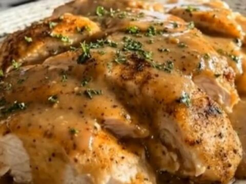 Sliced slow cooker chicken breasts drenched in glossy golden gravy garnished with fresh parsley