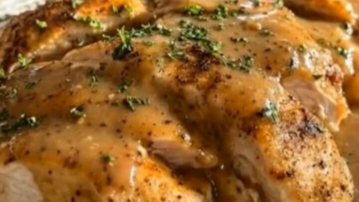 Sliced slow cooker chicken breasts drenched in glossy golden gravy garnished with fresh parsley