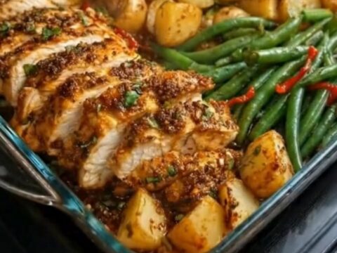 A glass baking dish filled with sliced herb-crusted chicken, roasted baby potatoes, and green beans.