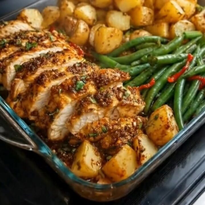 A glass baking dish filled with sliced herb-crusted chicken, roasted baby potatoes, and green beans.