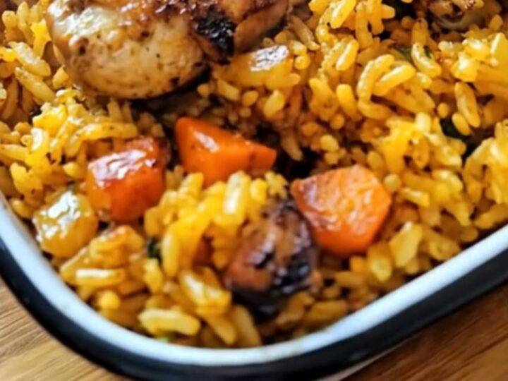 A close-up of a fork piercing juicy golden-brown chicken skin resting on vibrant yellow turmeric rice.