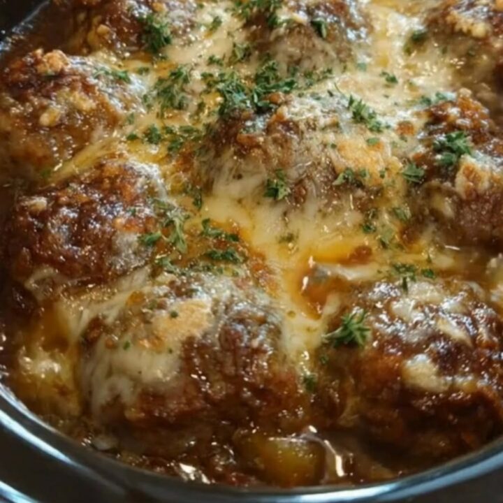 A black oval slow cooker filled with glazed meatballs under melted cheese and fresh parsley