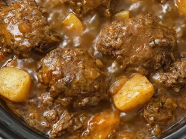 A steaming bowl of slow cooker meatball stew with tender meatballs and soft potato chunks in rich brown gravy