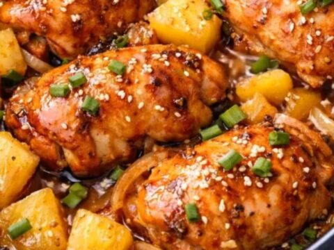 A close-up of tender, glossy slow cooker pineapple chicken garnished with fresh scallions and sesame seeds.