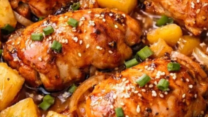 A close-up of tender, glossy slow cooker pineapple chicken garnished with fresh scallions and sesame seeds.