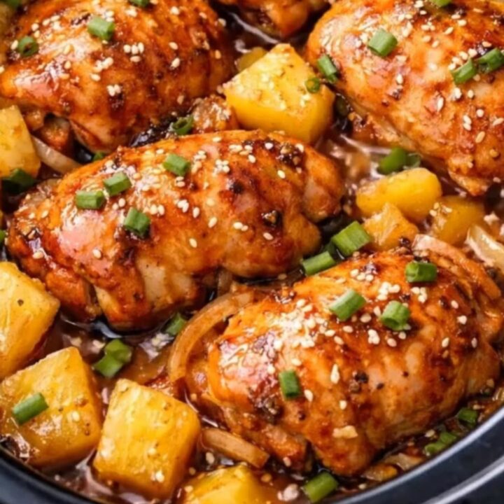 A close-up of tender, glossy slow cooker pineapple chicken garnished with fresh scallions and sesame seeds.