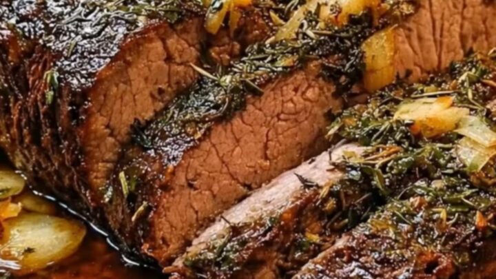 Sliced garlic herb roast beef in a dark roasting pan with caramelized onions and rich juices