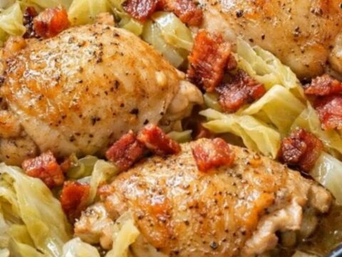 A black slow cooker filled with tender braised cabbage, golden bone-in chicken thighs, and crispy bacon bits.