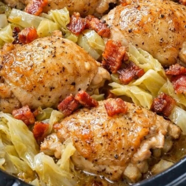 A black slow cooker filled with tender braised cabbage, golden bone-in chicken thighs, and crispy bacon bits.