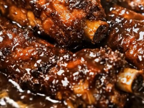 A stack of tender, slow-cooked baby back ribs glazed in a rich, glossy barbecue sauce in a slow cooker.