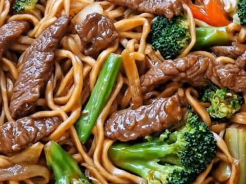 A steaming skillet of glossy beef stir fry noodles with tender seared beef and vibrant green broccoli.