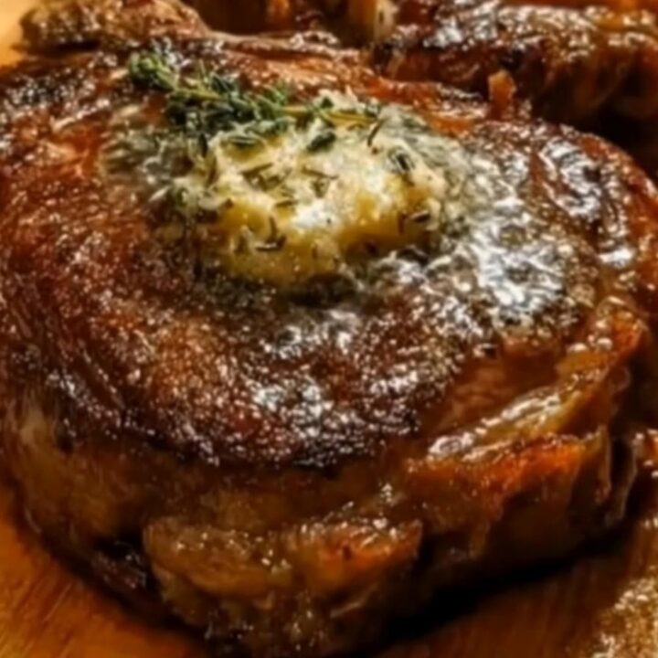 Two perfectly seared ribeye steaks resting on a wooden board topped with melting garlic herb butter and fresh thyme