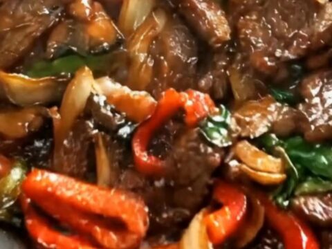 A hot skillet filled with tender seared beef strips and vibrant red bell peppers coated in a glossy brown glaze.