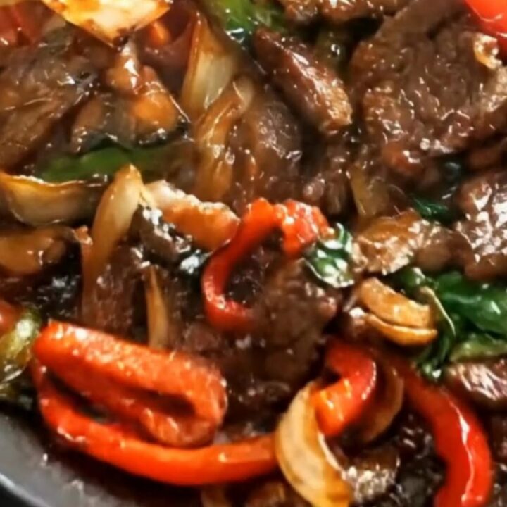 A hot skillet filled with tender seared beef strips and vibrant red bell peppers coated in a glossy brown glaze.