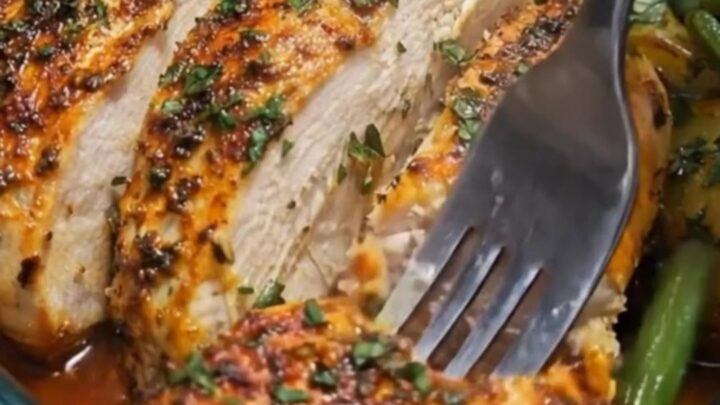 A glass baking dish filled with sliced herb-roasted chicken, golden baby potatoes, and tender green beans.