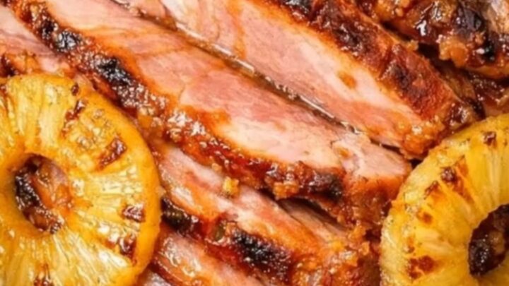 A glossy, caramelized spiral-cut ham surrounded by golden grilled pineapple rings inside a slow cooker.