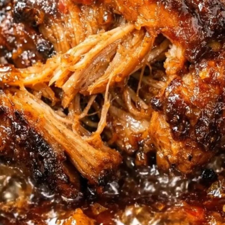 A close-up shot of glistening, sticky BBQ pulled pork piled high in a black slow cooker with steam rising.