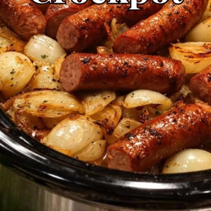 A close-up shot of juicy sliced sausages layered over golden caramelized onions inside a slow cooker.