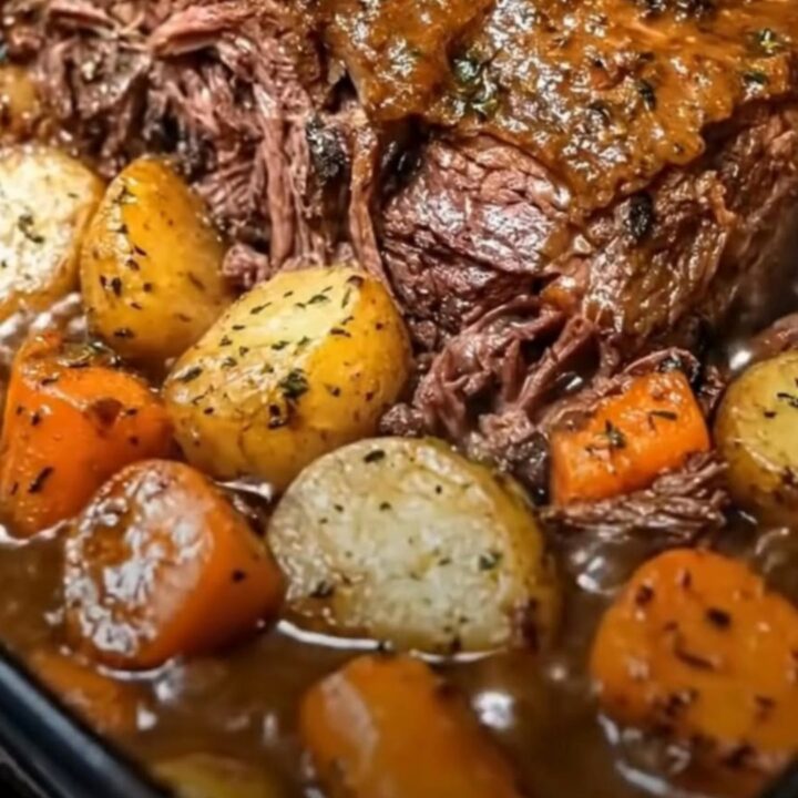 A caramelized beef pot roast surrounded by fork-tender baby potatoes and carrots in a baking dish