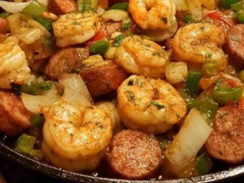A steaming black cast-iron skillet filled with juicy seasoned shrimp, sliced browned sausage, and colorful bell peppers.