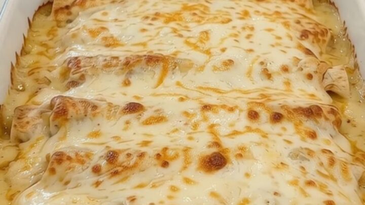 A spatula lifting a cheesy chicken burrito from a baking dish with a long, gooey cheese pull.