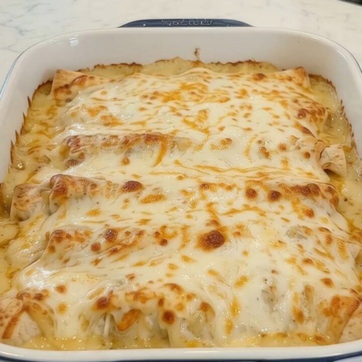 A spatula lifting a cheesy chicken burrito from a baking dish with a long, gooey cheese pull.