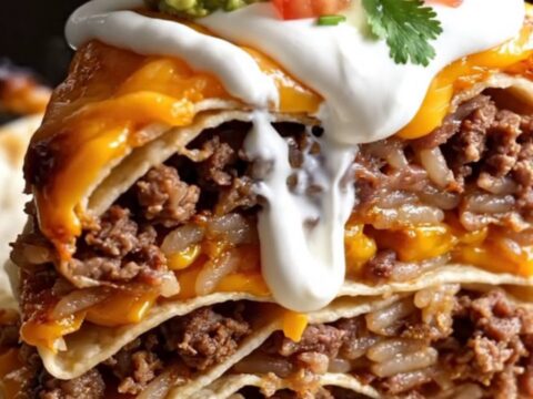 A close-up of a tall wedge of layered burrito bake showing beef, rice, beans, and melted cheese.