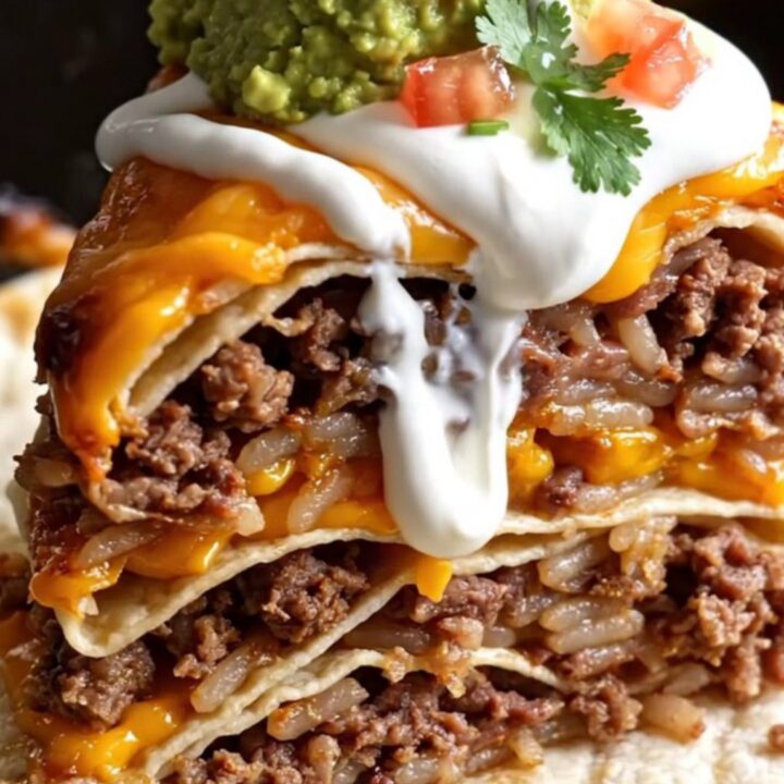 A close-up of a tall wedge of layered burrito bake showing beef, rice, beans, and melted cheese.