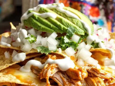 A steaming, rustic red ceramic slow cooker filled with cheesy, saucy chilaquiles topped with fresh avocado and cilantro.