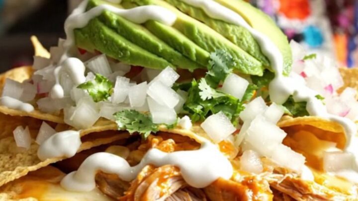 A steaming, rustic red ceramic slow cooker filled with cheesy, saucy chilaquiles topped with fresh avocado and cilantro.