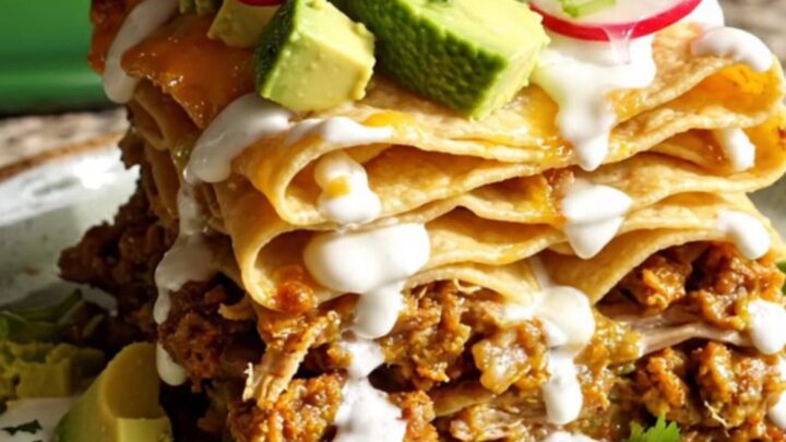 A tall slice of slow-cooked pork and hominy enchilada casserole topped with fresh avocado and cilantro.