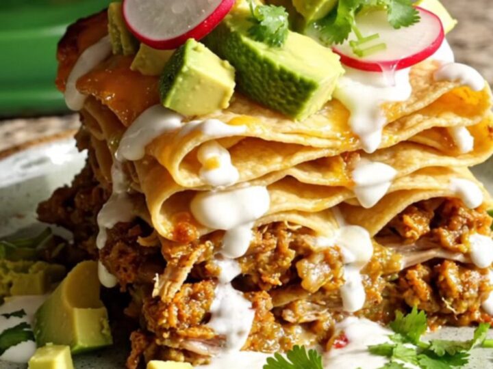 A tall slice of slow-cooked pork and hominy enchilada casserole topped with fresh avocado and cilantro.