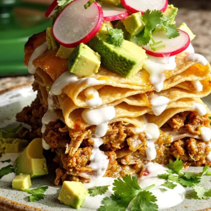 A tall slice of slow-cooked pork and hominy enchilada casserole topped with fresh avocado and cilantro.