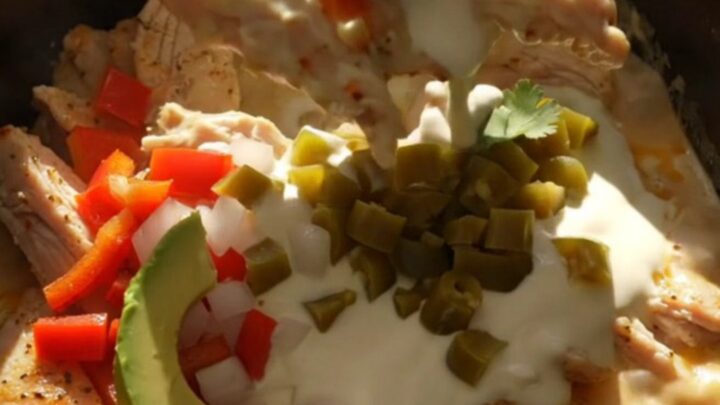 A close-up shot of creamy Pollo con Queso in a black slow cooker with bubbling white cheese.