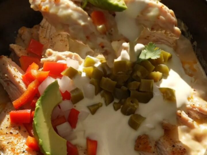 A close-up shot of creamy Pollo con Queso in a black slow cooker with bubbling white cheese.